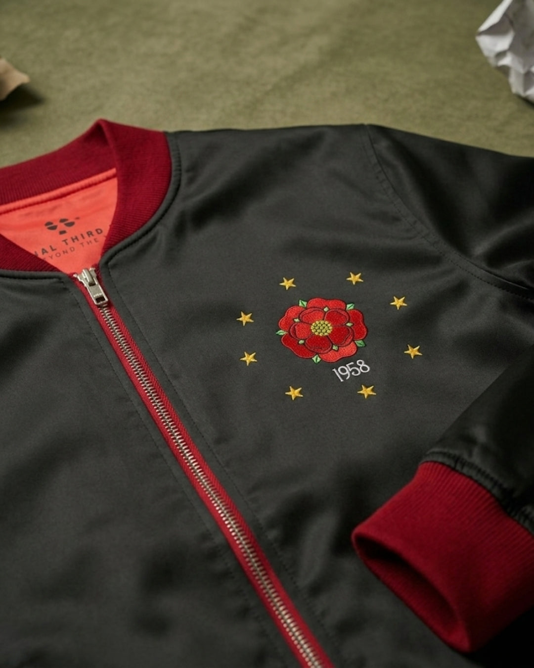 Black jacket with red zipper and embroidered design on a green surface