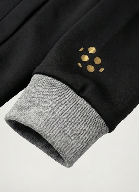 Close-up of a black garment with gold hexagonal pattern on a light gray background