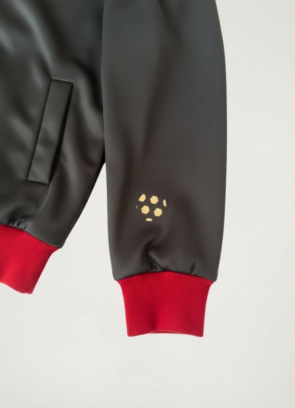 Close-up of a dark gray sleeve with red cuffs and a small yellow logo on a light gray background