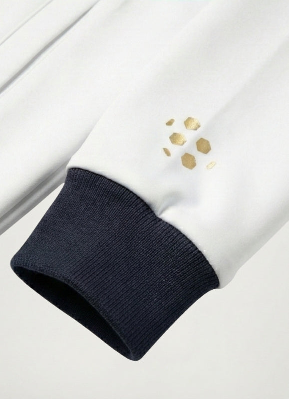 Close-up of a white garment with gold accents and navy cuffs on a light gray background