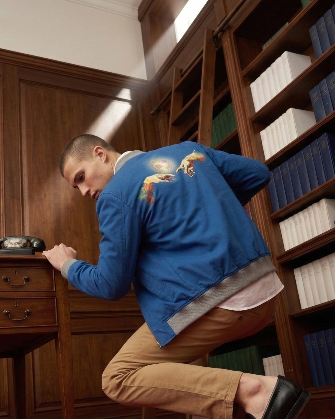 Man in a blue jacket with a colorful design in a room with wooden furniture and bookshelves.