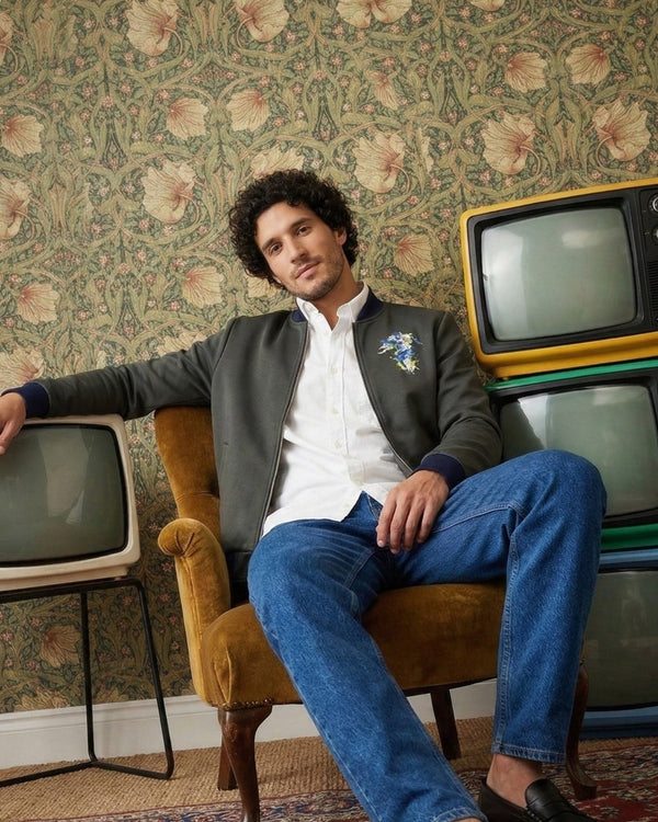 Man sitting on a vintage armchair with stacked old TVs against a floral wallpapered wall.