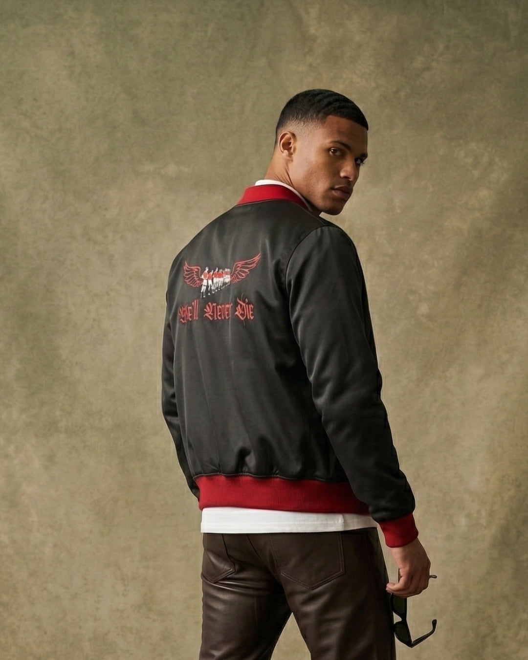 Man wearing a black and red jacket with text on the back against a textured beige wall.