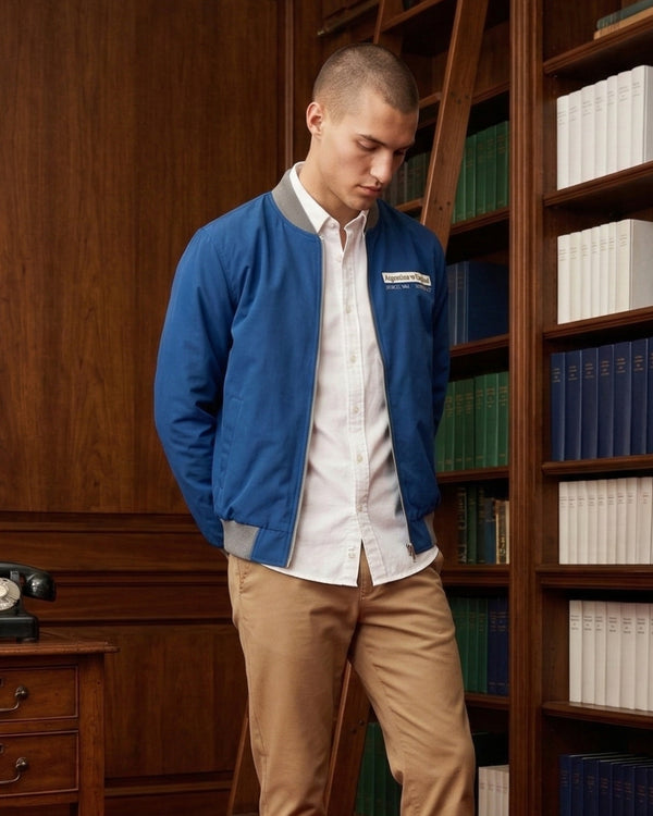 Man wearing a blue jacket with a logo in a room with wooden bookshelves.