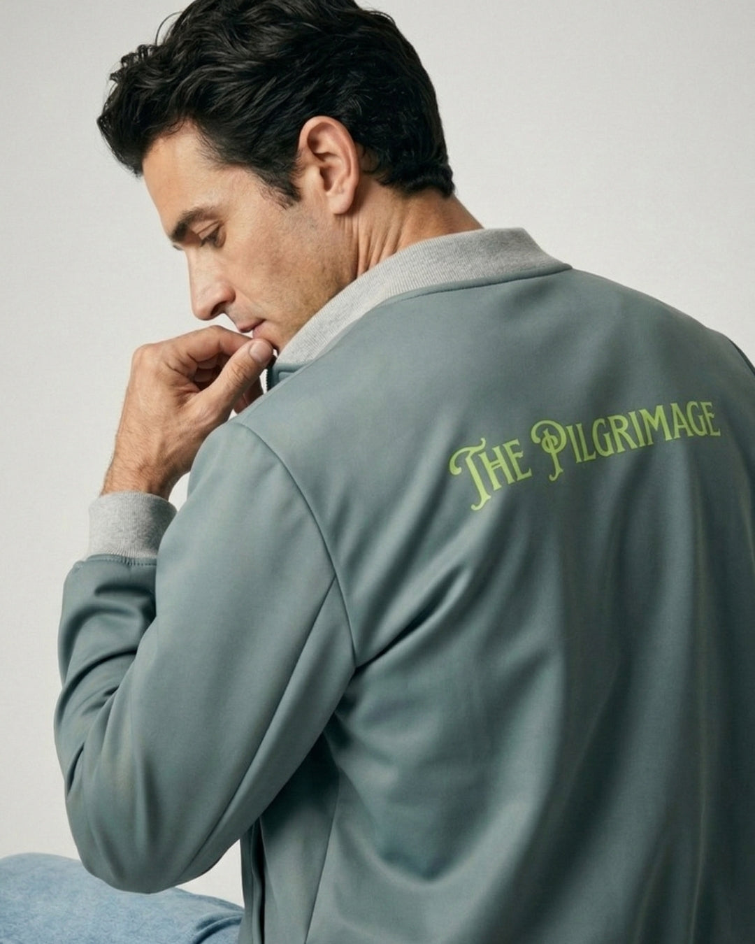 Man wearing a gray jacket with 'The Pilgrimage' logo on the back, looking away from the camera.