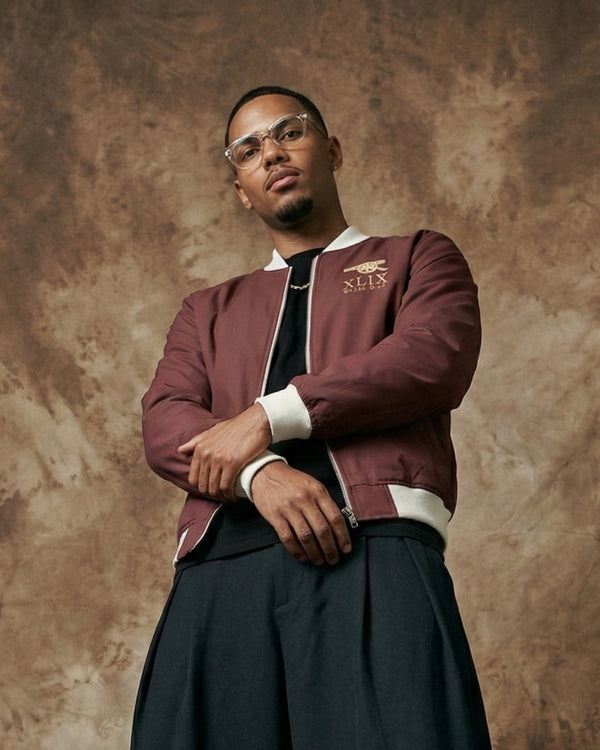 Man wearing a maroon jacket with a logo on a textured brown background