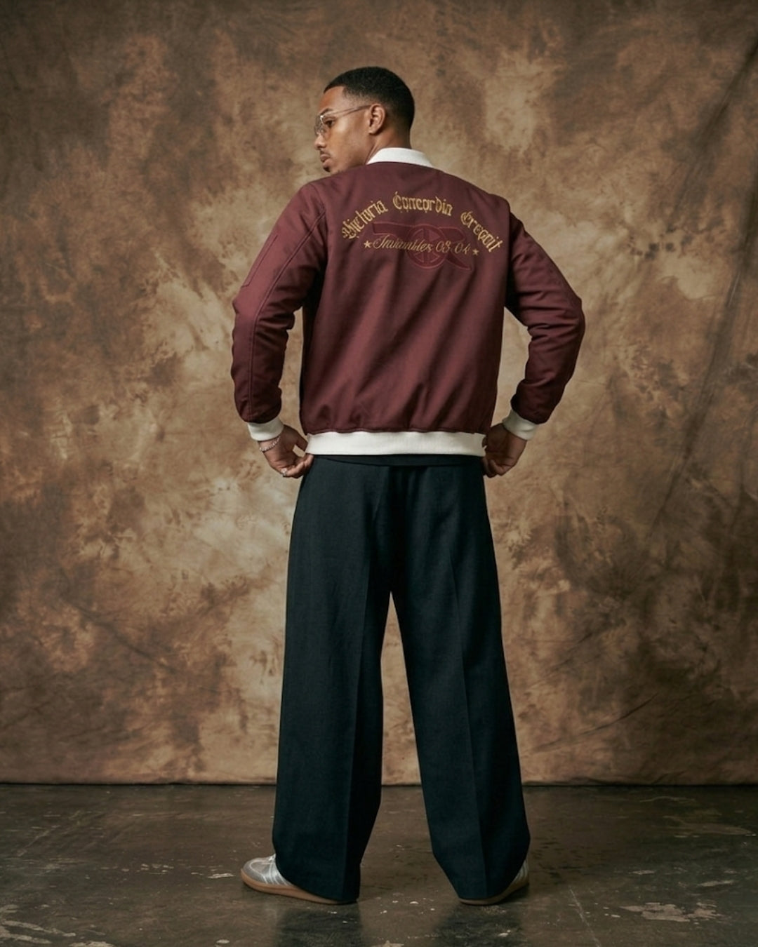 Man wearing a maroon varsity jacket with text on the back against a textured brown background