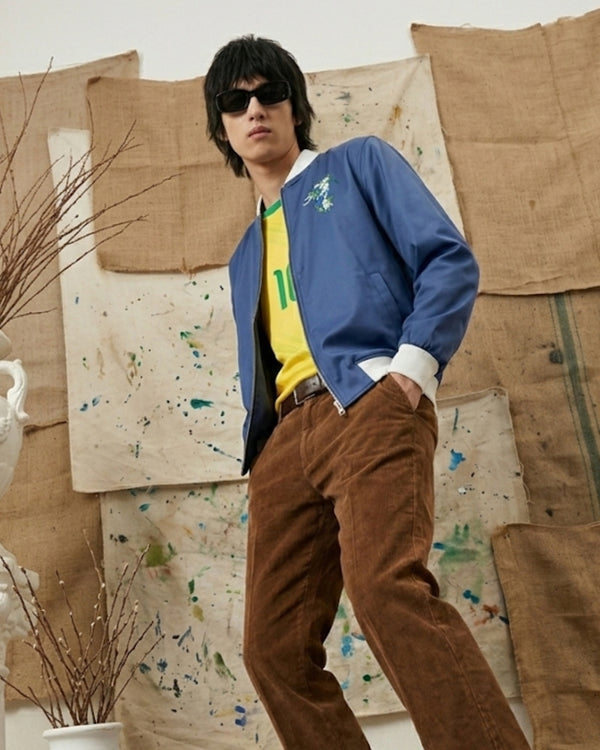 Person wearing a blue jacket and brown pants standing in front of textured walls.